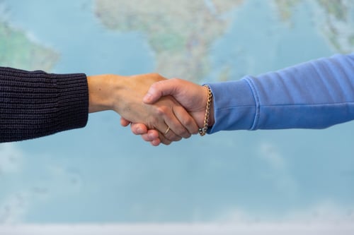 A photo of two hands performing a handshake in front of a map